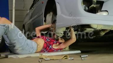 穿着破牛仔裤和格子衬衫的金发女孩躺在车下，在<strong>服务站</strong>修理
